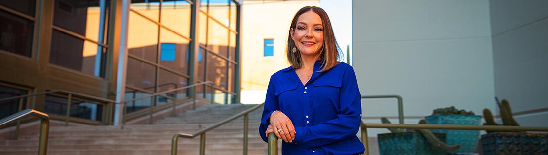 Professional woman smiles on steps of Northwest Campus in a blue blazer.